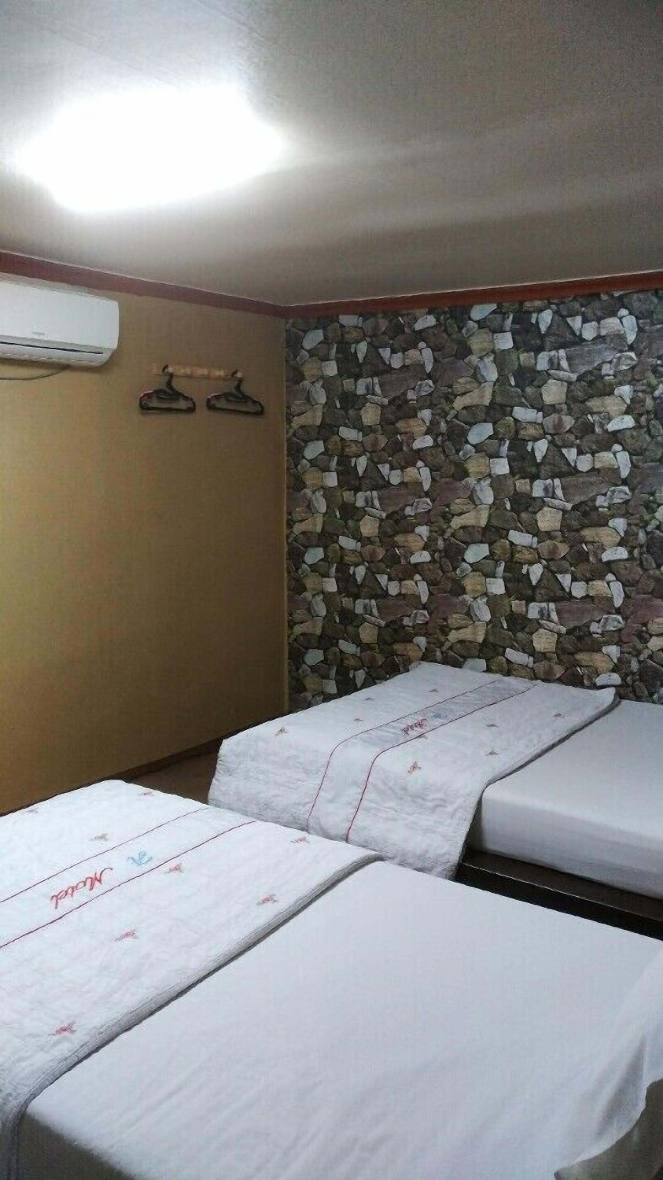 A room with two beds, a stone wall, and an air conditioning unit.