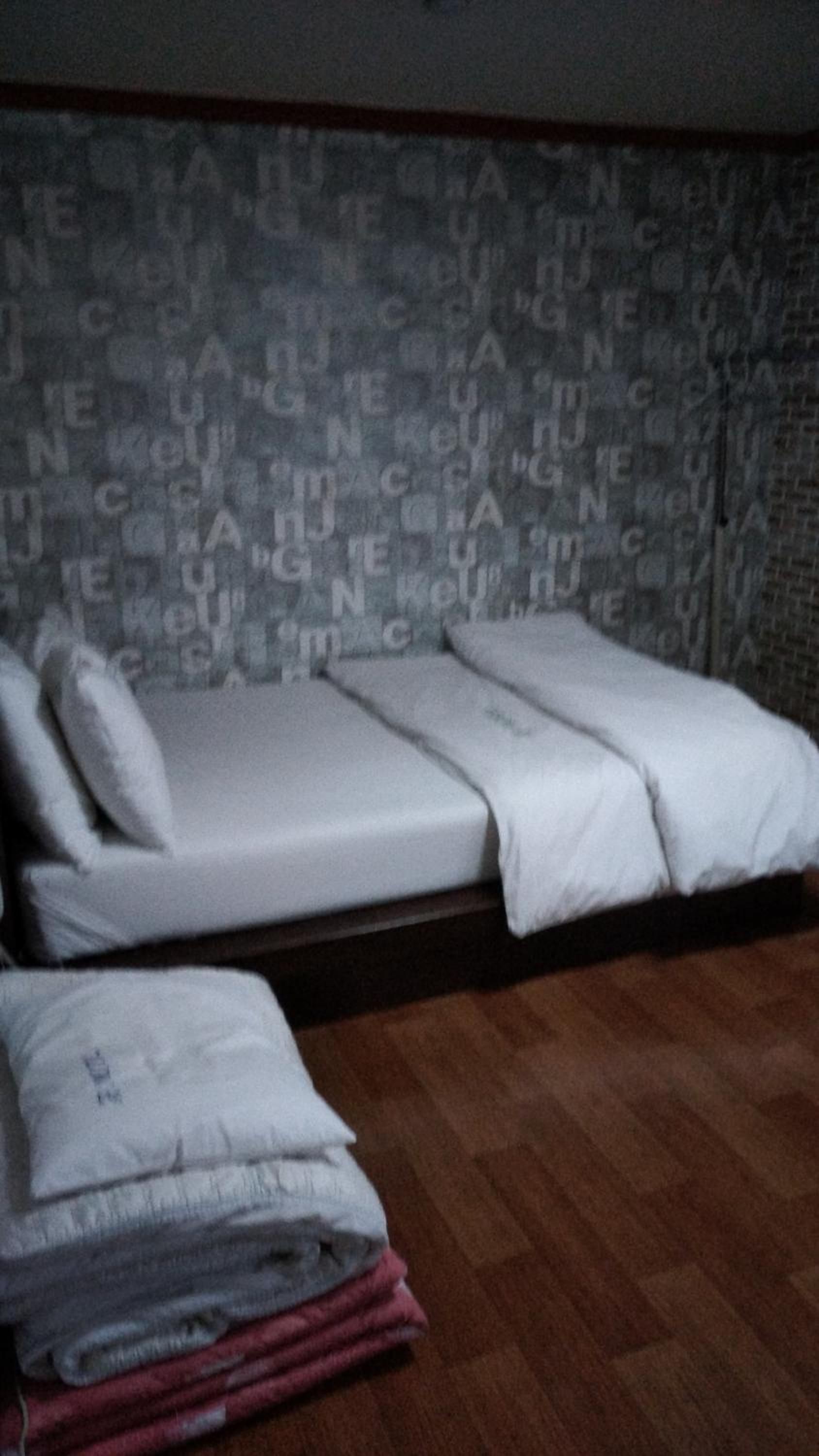Una habitación con una cama, una mesita pequeña y una pared con un diseño repetido.