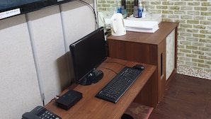 A wooden desk with a computer setup, including a monitor, keyboard, and phone. - Gumi A Motel (Gumi)