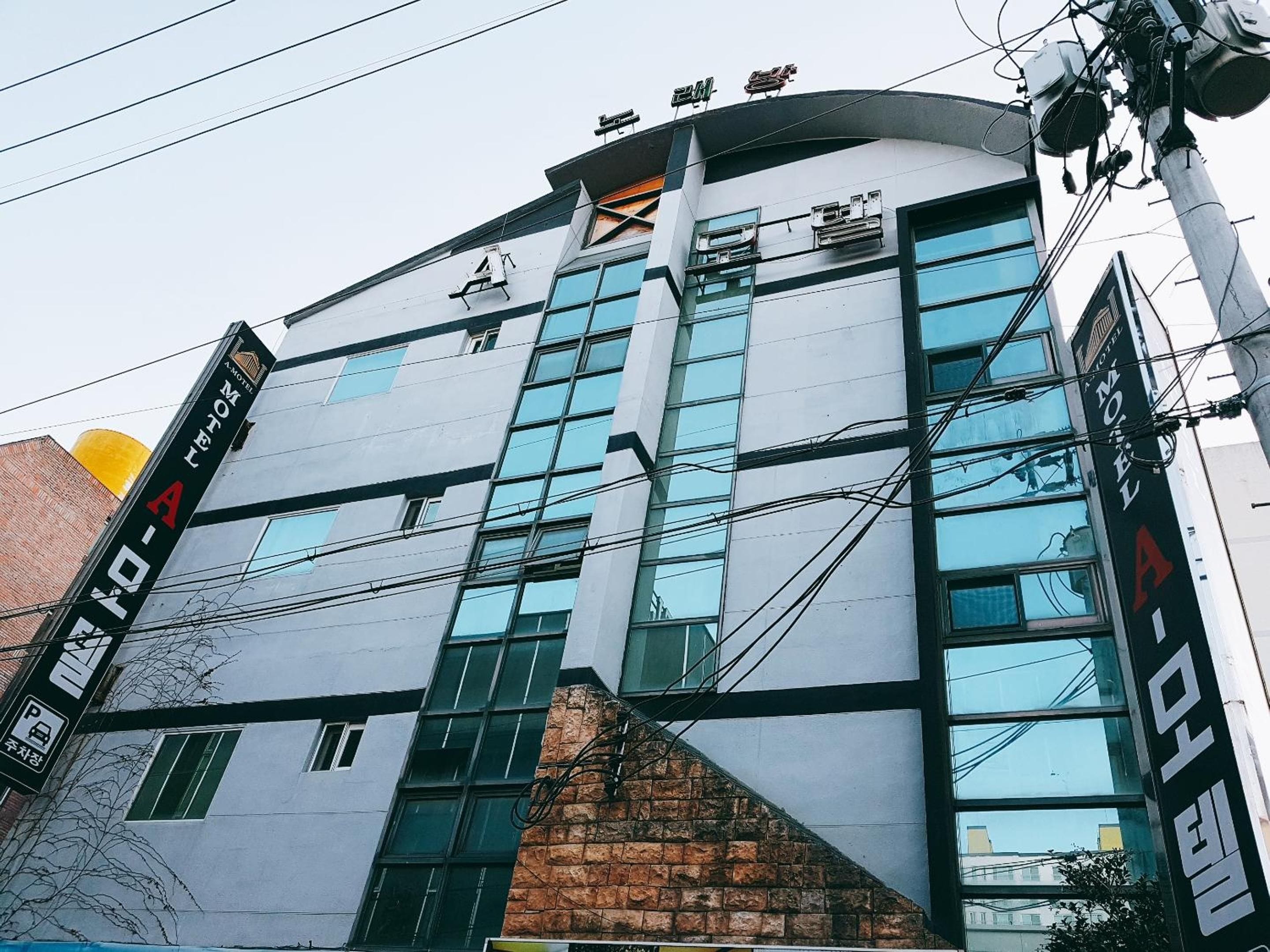 Un edificio moderno con múltiples ventanas, una sección de ladrillo y señalización para un hotel y estacionamiento.