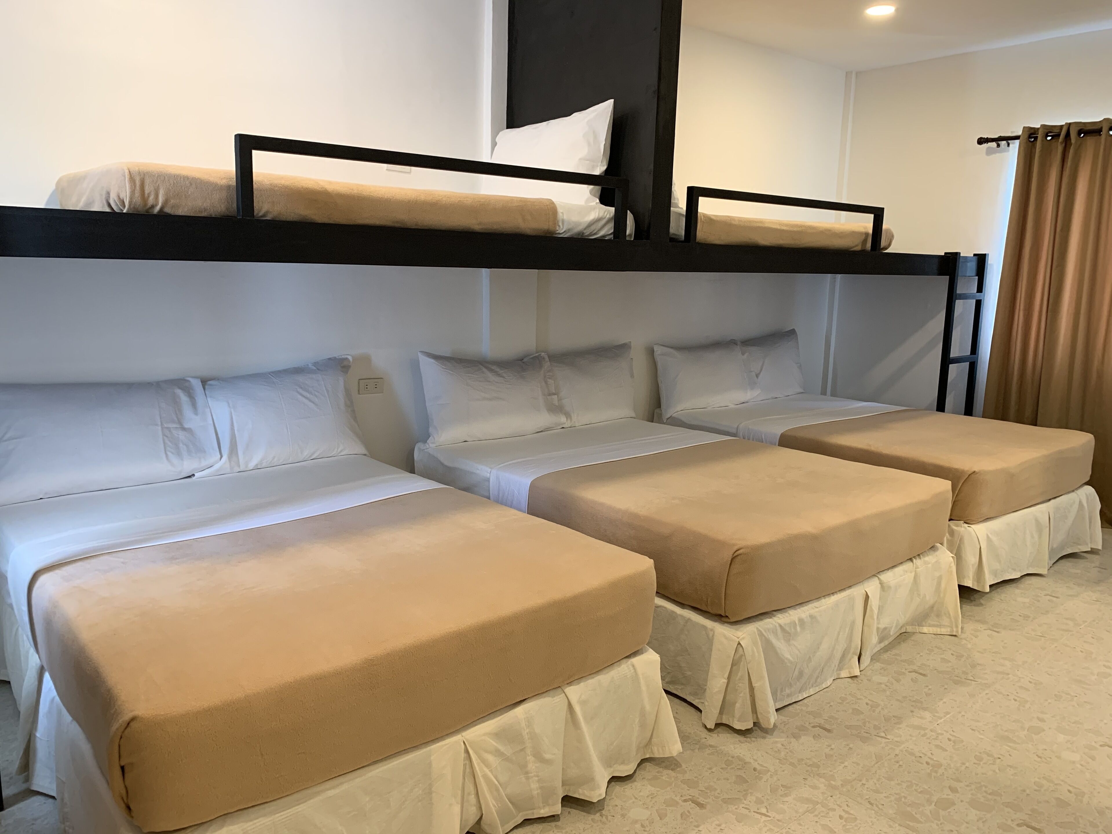 A room with four beds arranged in a row, each with a headboard and footboard. There is a ladder against the wall on the right side.