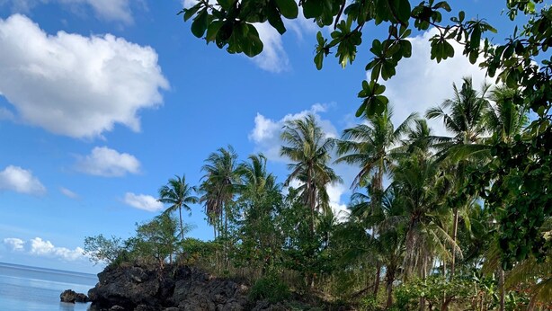 A beach with lounge chairs and a rocky outcrop.