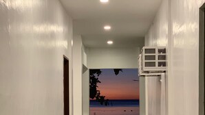 A hallway with a view of a sunset over the ocean, white walls, and a concrete floor.