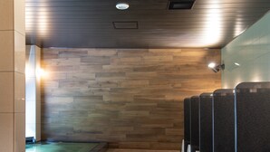 Eine Toilette mit Holzwandverkleidung, einem grünen Boden und schwarzen Urinalen.