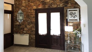 Un mur en pierre, une porte à deux battants avec un rideau blanc, un radiateur et un objet décoratif accroché au mur.