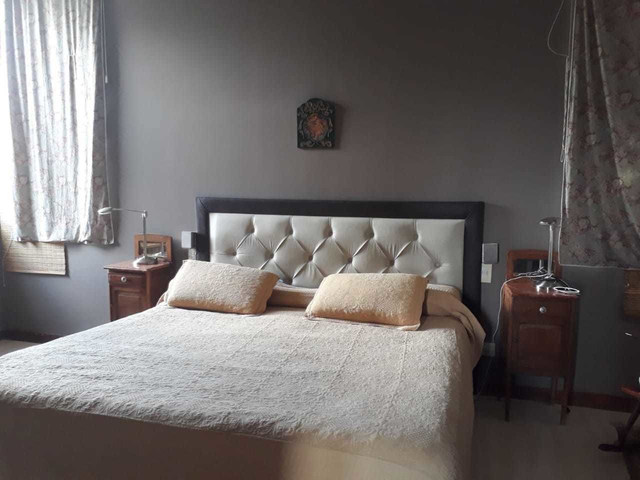 Un dormitorio con cabecera capitonada, dos mesitas de noche, cama con edredón texturizado y un adorno en la pared.