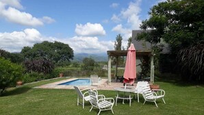 Un jardin avec une piscine, du mobilier d’extérieur et une pergola surmontée d’un parasol rose.