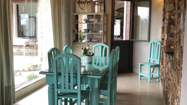 Un espace repas avec des chaises de couleur turquoise et une table en verre, un mur en pierre et un plafond en bois.