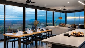 A modern dining area with a large table set for six, a sofa, and a view of the countryside. - Sky High: stunning, iconic, dramatic (Mount Franklin)