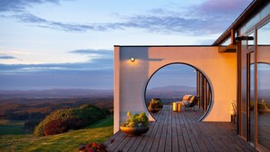 A modern house with a wooden deck, a large circular window, and a view of the landscape. - Sky High: stunning, iconic, dramatic (Mount Franklin)