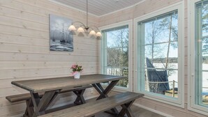 En inredning med träpanel, ett stort bord och bänkar, stora fönster och en taklampa.