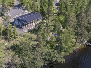Une maison à deux étages dotée d’un balcon, entourée d’une forêt dense et bordée d’un plan d’eau.