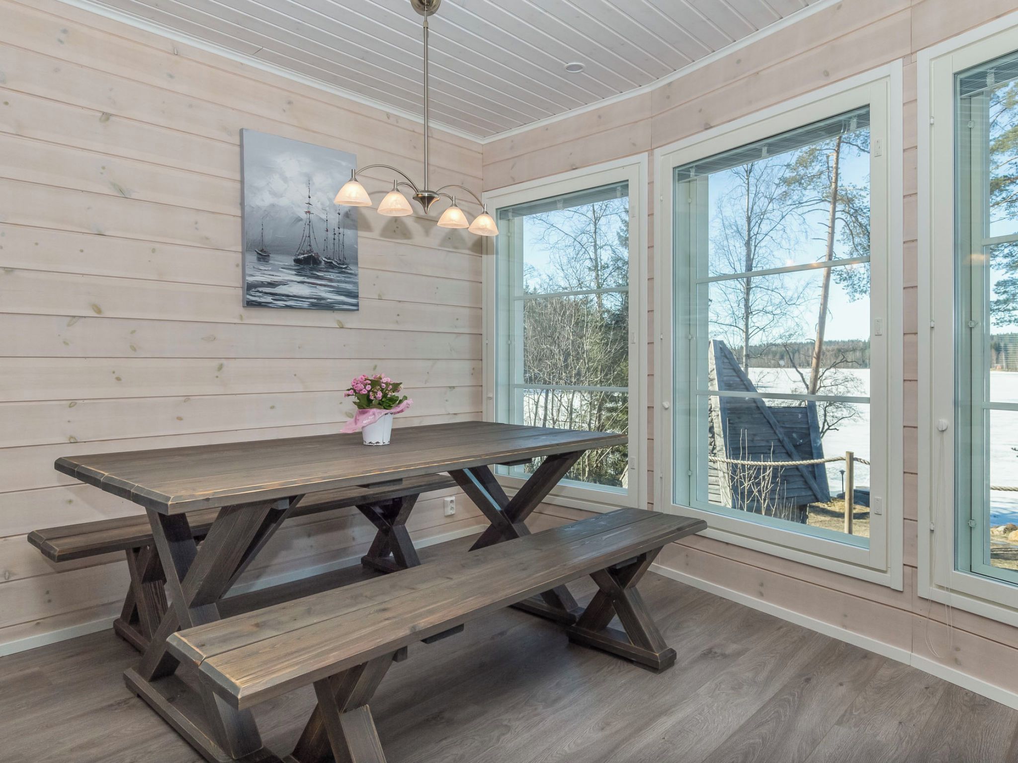 Puisesti sisustettu tila, jossa on pöytä ja penkit, suuret ikkunat ja kattovalaisin.