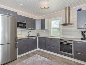 Une cuisine moderne dotée d’appareils électroménagers en acier inoxydable, de meubles de rangement gris et d’une fenêtre équipée de stores.