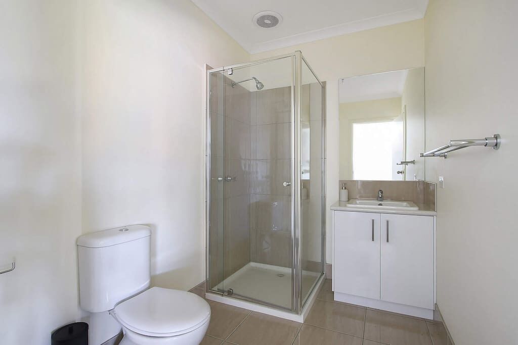 A bathroom with a toilet, a glass-enclosed shower, and a sink with a mirror.