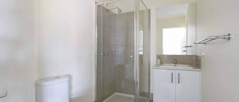 A bathroom with a toilet, a glass-enclosed shower, and a sink with a mirror.