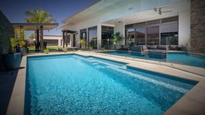 Un espace piscine extérieur moderne, doté d’un coin salon couvert et d’une grande baie vitrée donnant sur la piscine.