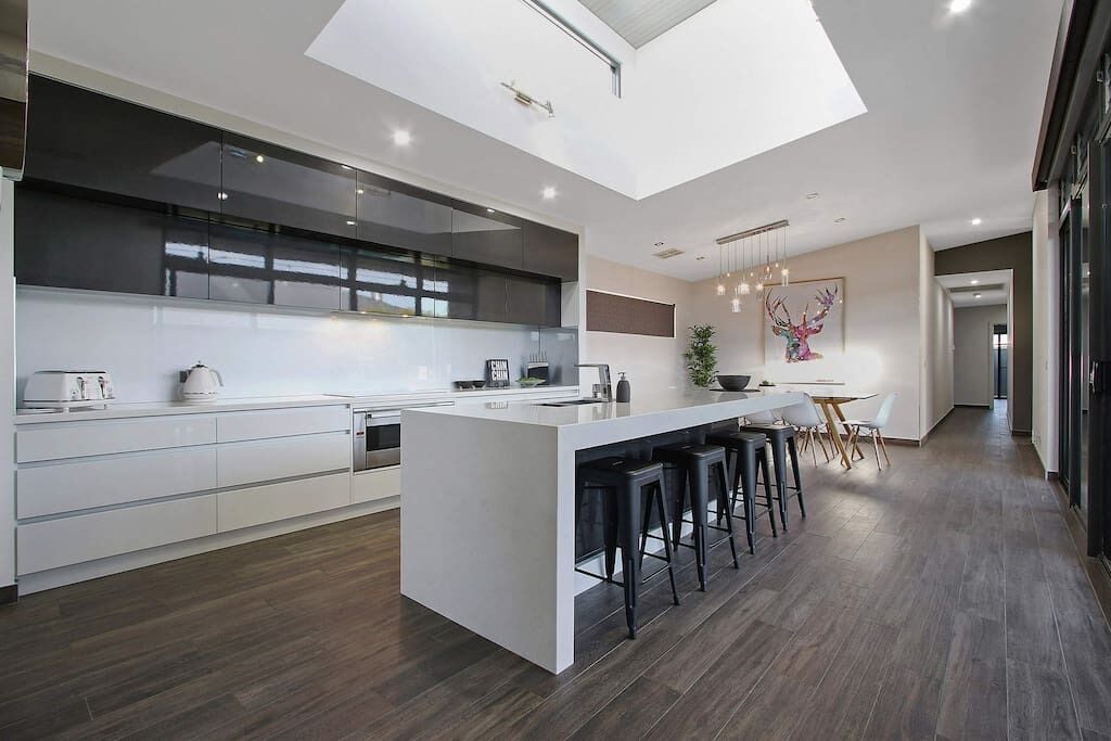 Een moderne keuken met een centraal eiland, barstoelen en een eethoek met een tafel en stoelen.