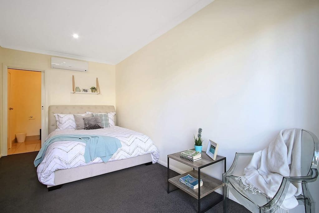 Un dormitorio con cama, mesita de noche, silla y puerta.