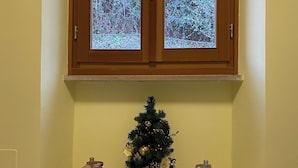 Ein Holzkabinett mit Milchglasschränken, eine kleine Weihnachtstanne im Korb und zwei Laternen auf einem Kachelboden.