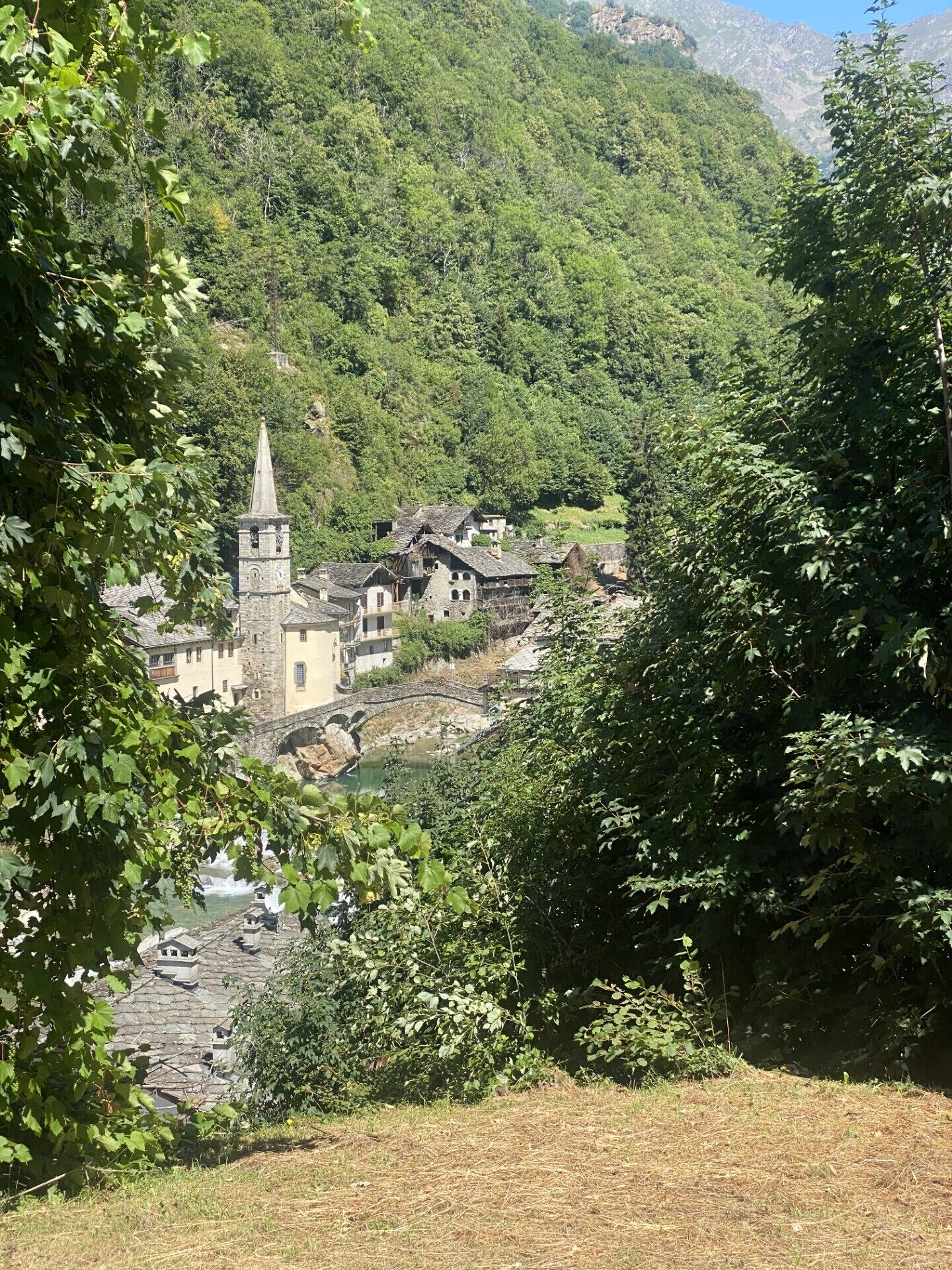 Un village historique avec des bâtiments en pierre, un clocher d’église et une rivière.