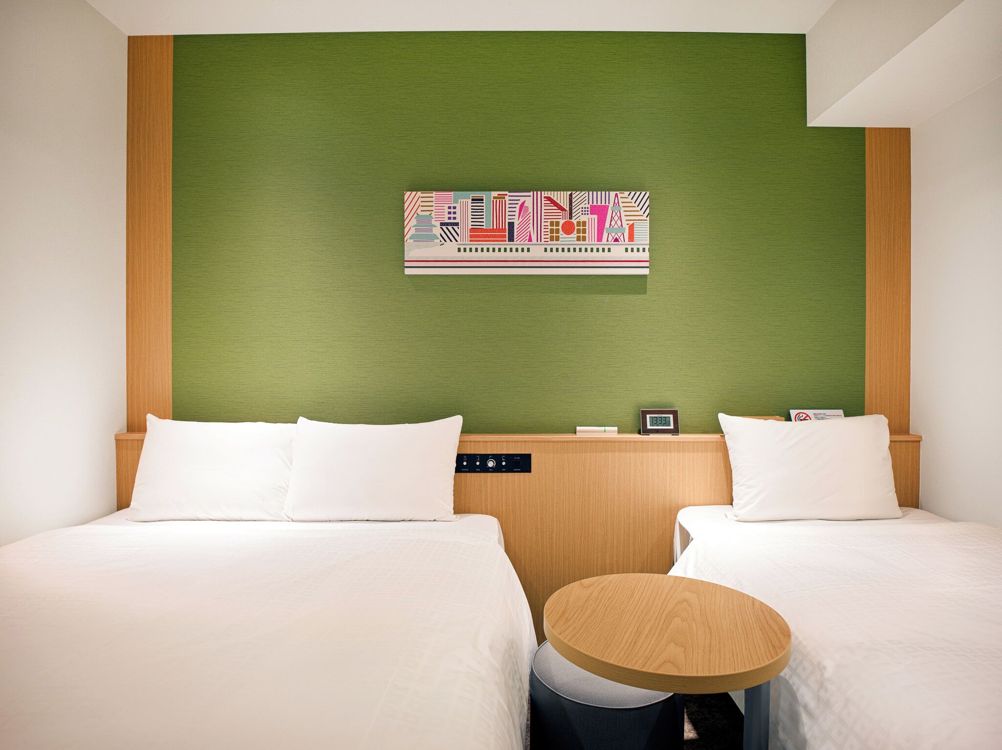 Habitación de hotel con dos camas, una pared verde decorativa, un reloj y una mesita.