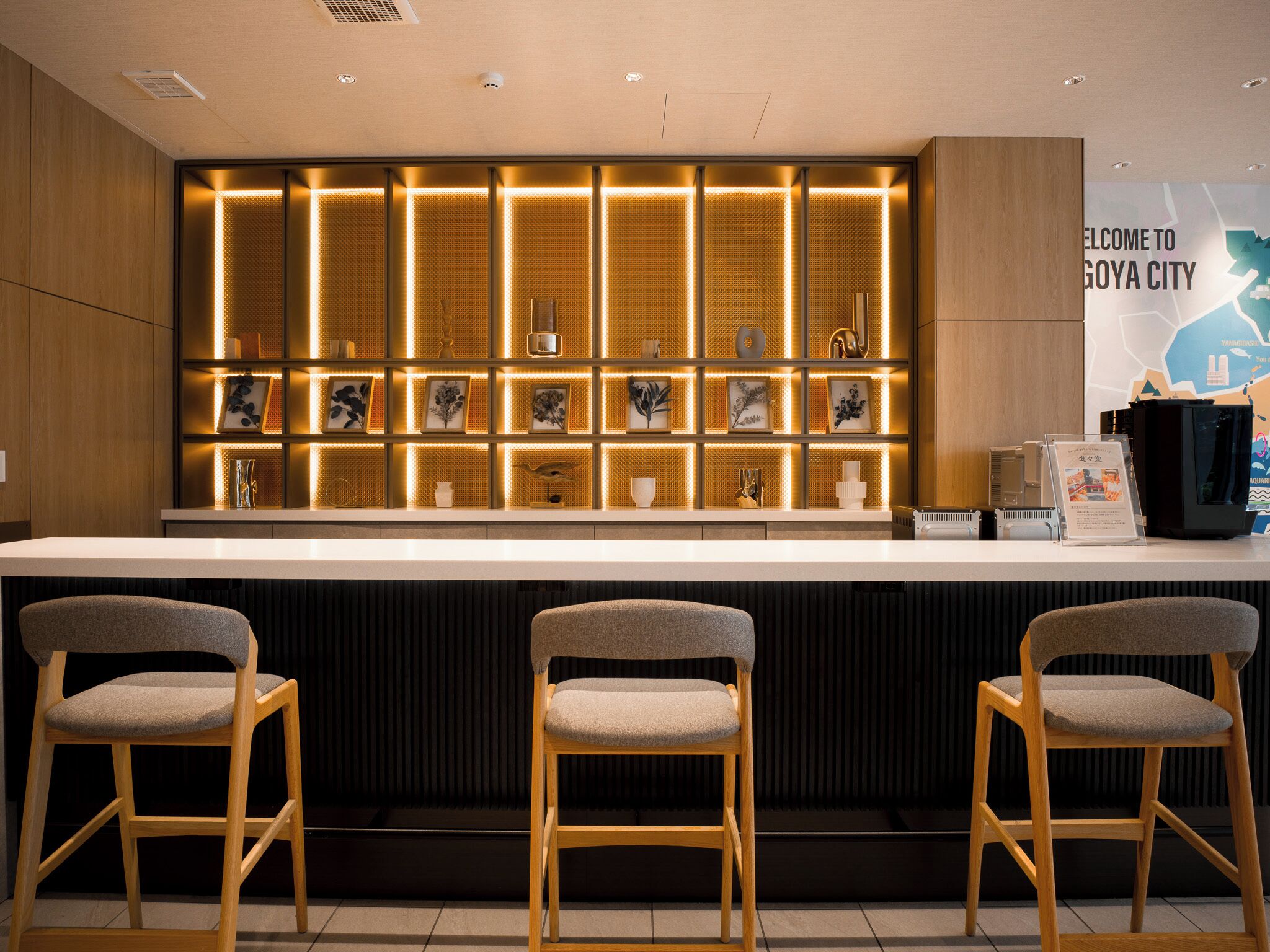 A reception area with a counter, three wooden chairs, and a wall with illuminated panels and framed pictures.