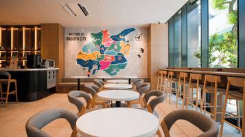 Ein modernes Café-Interieur mit runden Tischen, grauen Stühlen, einer Wand mit einer Karte und Blick ins Grüne.