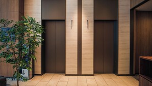 A modern elevator with a minimalist design, a potted plant, and a wooden panel wall. - SONO Moon Nagoya  (Nagoya)
