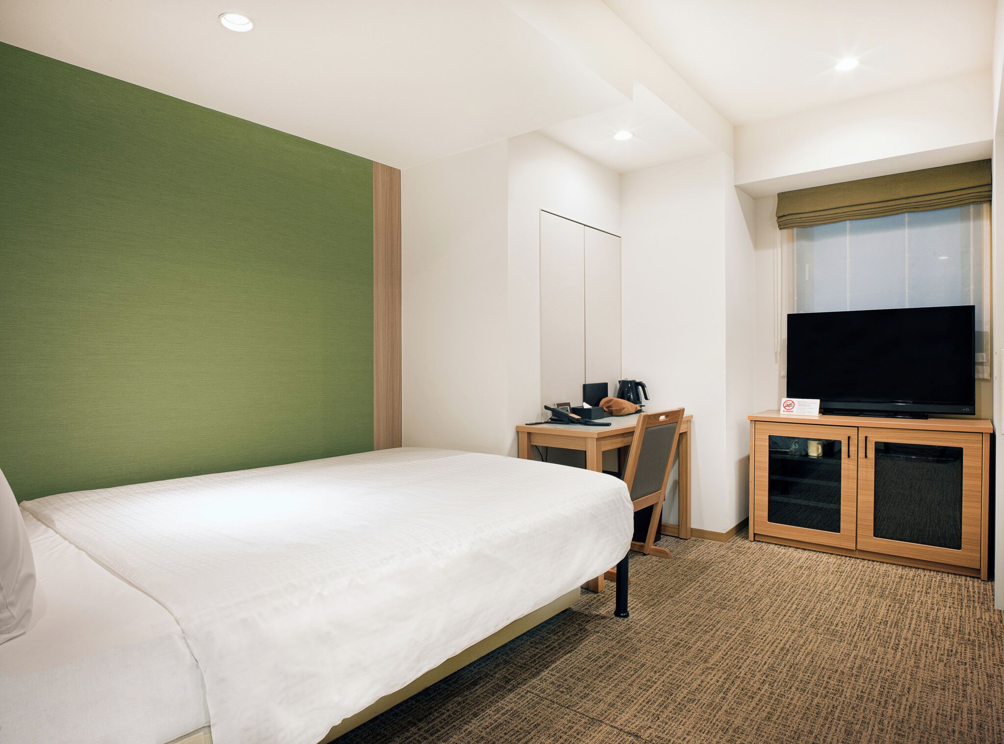 A hotel room with a bed, a desk with a chair, a television, and a cabinet.
