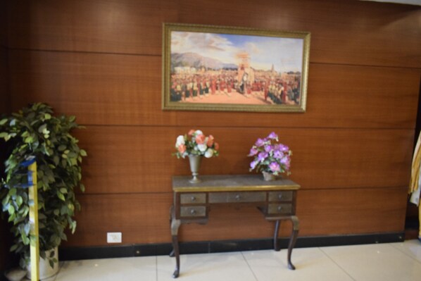 A wooden wall with a framed painting, a potted plant, and a small table with two vases of flowers.