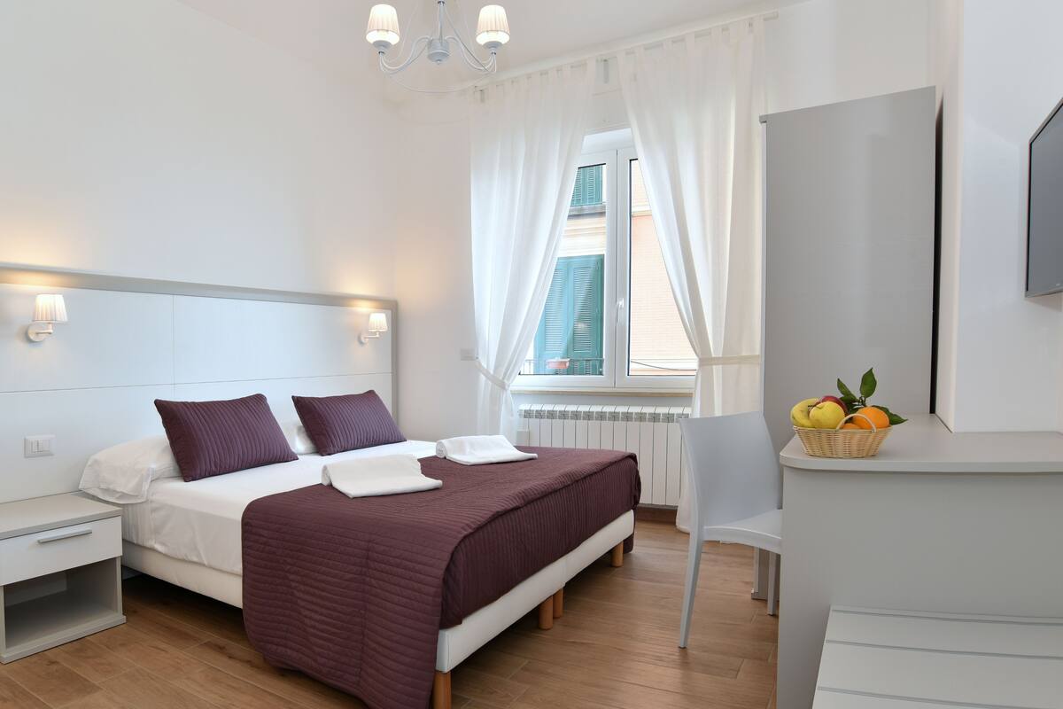 A modern bedroom with a bed, bedside tables, a desk, and a window with curtains.