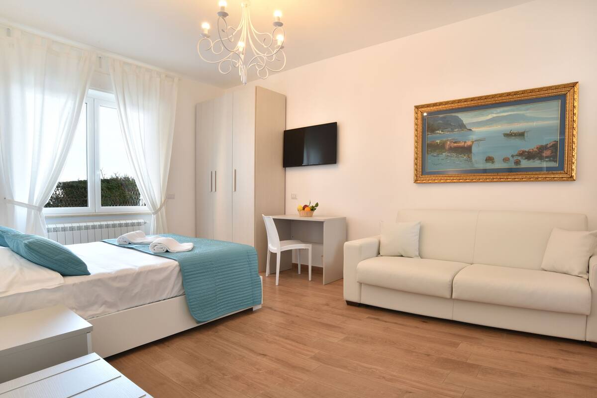 A bedroom with a bed, a desk, a white sofa, and a painting on the wall.