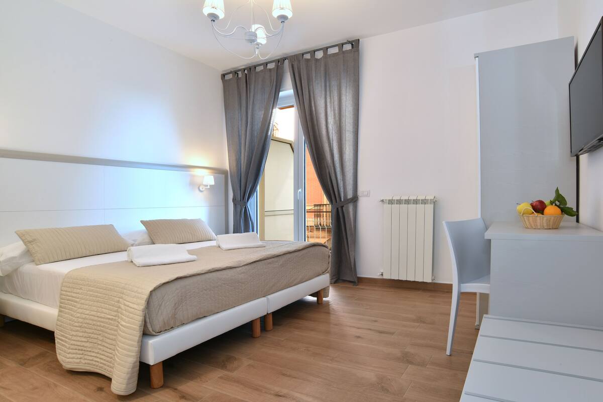A bedroom with a bed, a desk, a chair, a television, and a window with curtains.