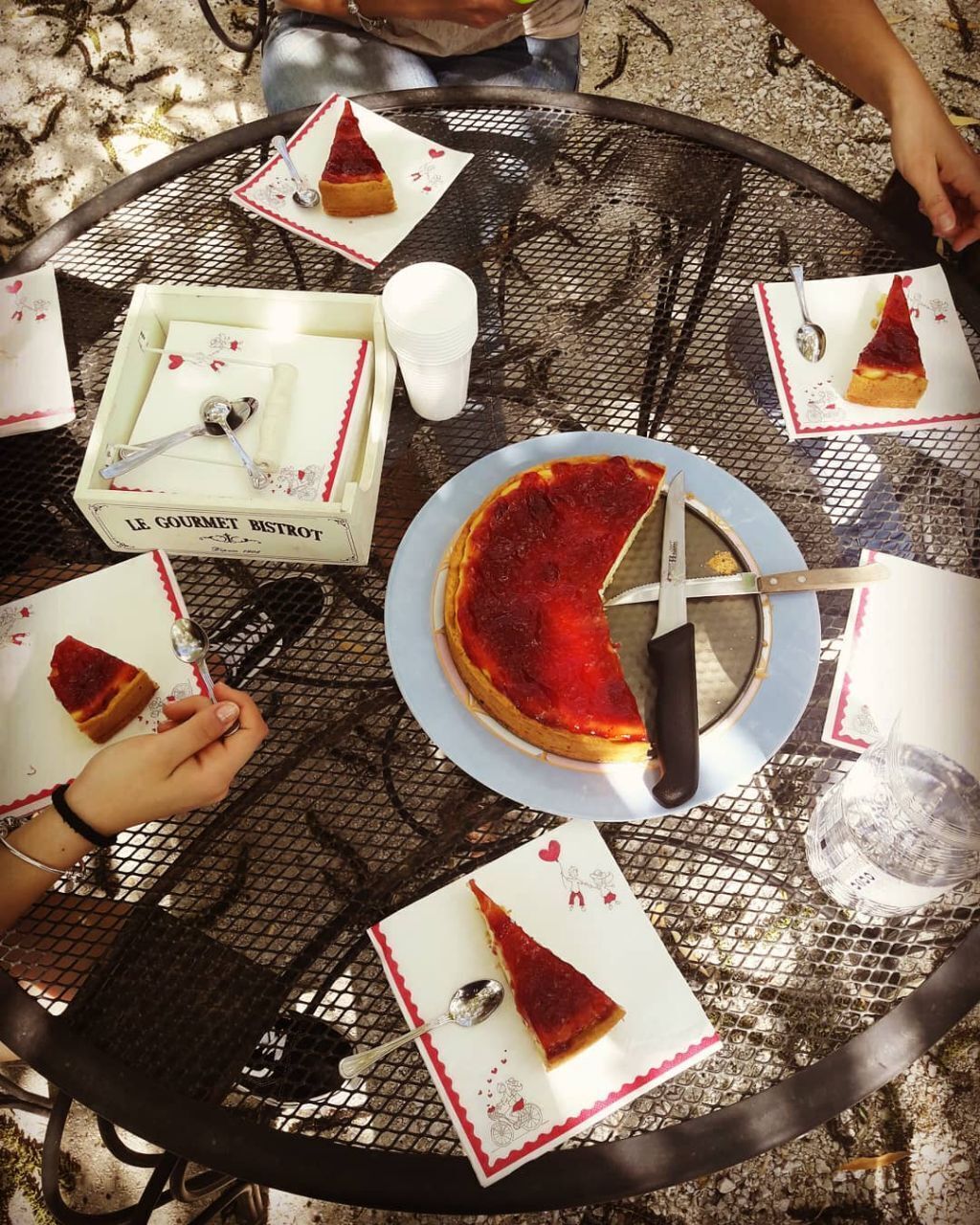 A round metal table with a pizza and a knife on it, surrounded by plates with pizza slices and napkins.