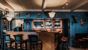 Una zona de bar con taburetes de madera, un mostrador con vitrina de vidrio y cuadros en las paredes.