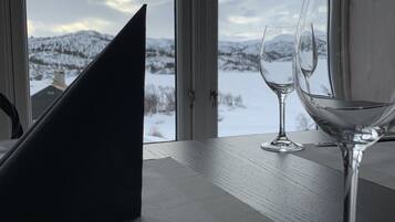 Una mesa con un cuchillo, dos copas de vino y un holder negro para servilletas junto a una ventana con vistas a una montaña nevada.