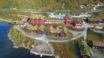 A cluster of red-roofed buildings with a lake and forested area in the background.