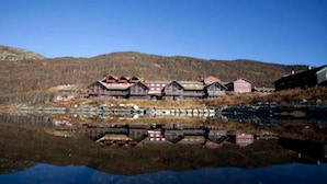 Zona de cabañas junto al lago con varias construcciones de madera, algunas con techos rojos, reflejándose en el agua.