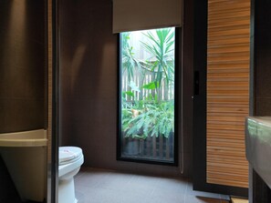A modern bathroom with a toilet, a window with a view of a garden, and a wooden panel wall. - Roppongi Motel (Pingtung)