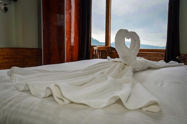 A bed with a white blanket and a towel shaped like a heart.