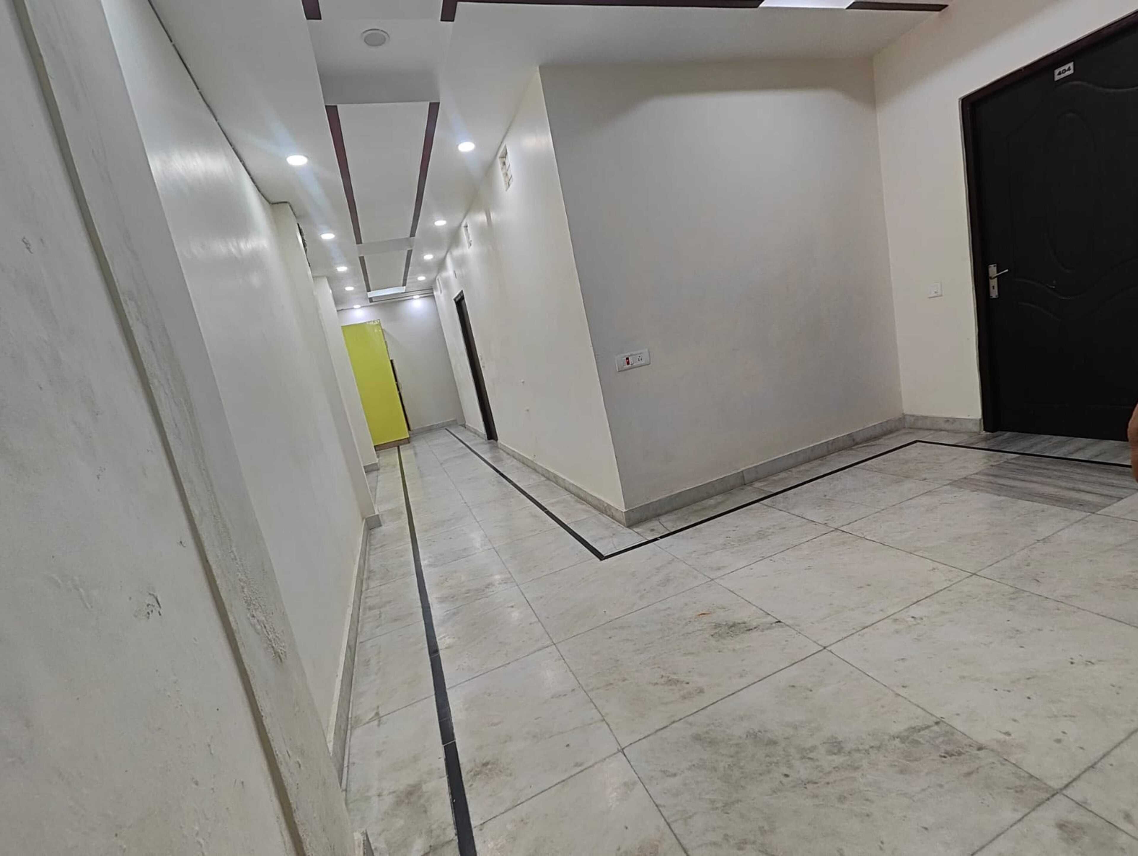A corridor with white walls, a tiled floor, and a black door on the right.