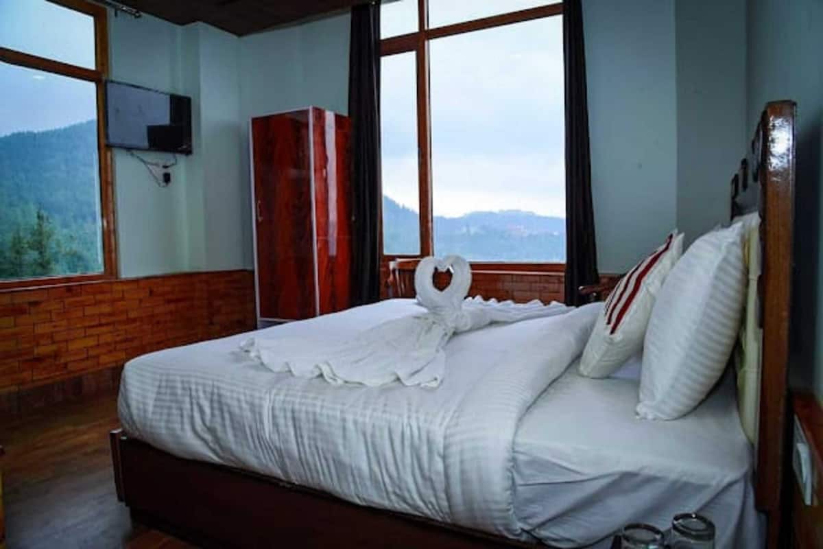 A bed with a white comforter and pillows, a wooden headboard, and a TV mounted on the wall.