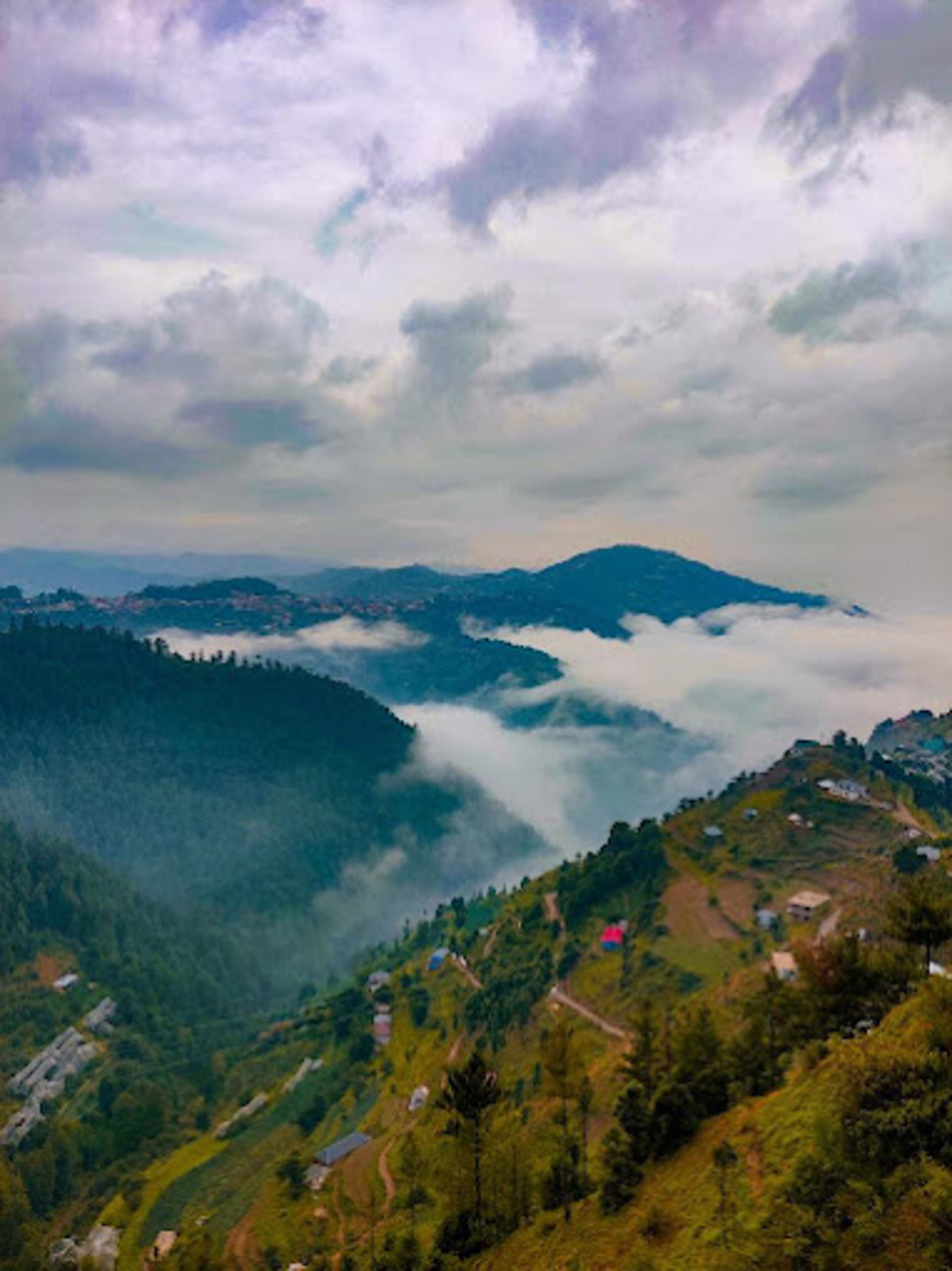 A mountainous landscape with a valley, scattered houses, and a road.