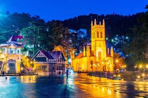A historic town square with a prominent church featuring a tall bell tower, a traditional building with a sloped roof, and a modern structure with a glass facade.