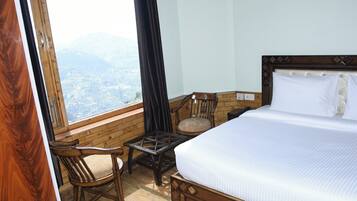 A bedroom with a large bed, a wooden chair, a small table, and a view of the mountains through a window.
