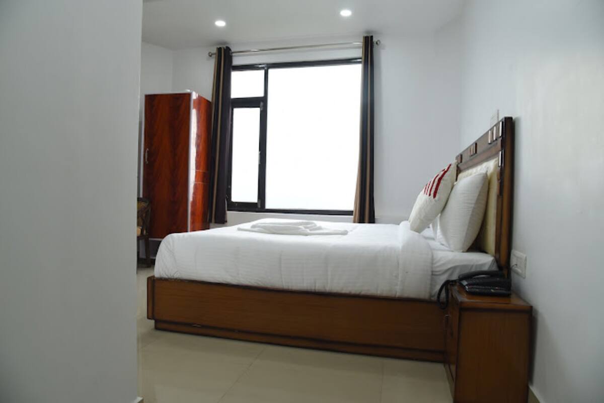 A bedroom with a wooden bed, a nightstand, a wardrobe, and a large window with curtains.