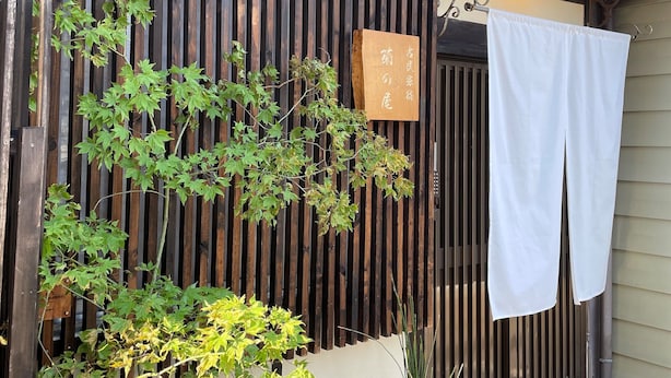 Un edificio de estilo japonés tradicional con un muro de listones de madera, un farol colgante y un letrero.