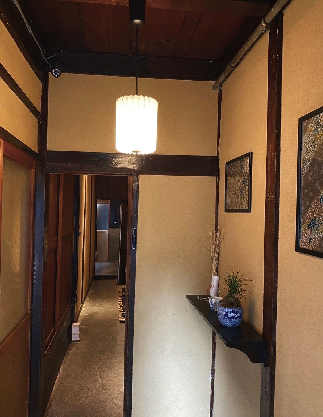 A hallway with a wooden ceiling, a hanging light fixture, and a small table with a vase and plant.