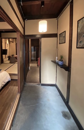 A narrow hallway with a wooden ceiling, a light fixture, and a small shelf with decorative items. - Kikunoya (Nagoya)